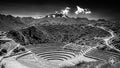 Black and white photo of Incan terraces at Moray with a snow-capped mountain and drifting clouds in the background.