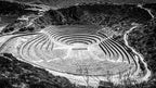 Circular Incan terraces in Moray, Peru, captured in black and white from above, with shadows accentuating the crater-like dep