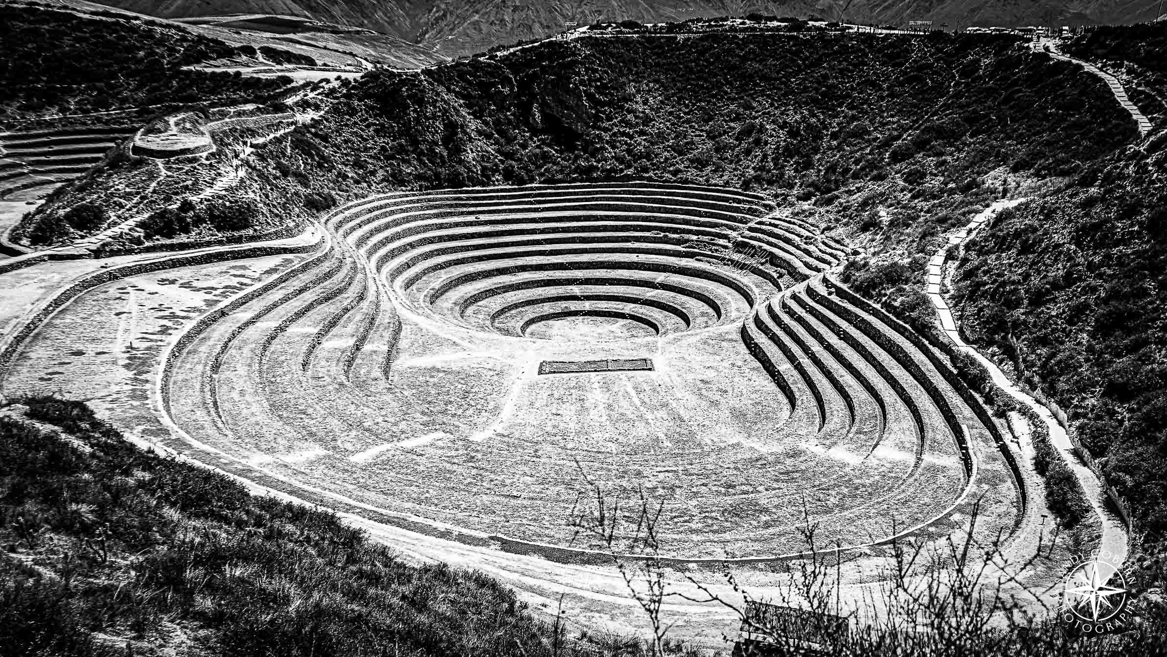 Circular Incan terraces in Moray, Peru, captured in black and white from above, with shadows accentuating the crater-like dep