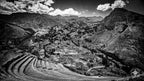 A bird’s-eye view of ancient Incan terraces carved into a steep mountain slope, descending toward a valley where modern vil