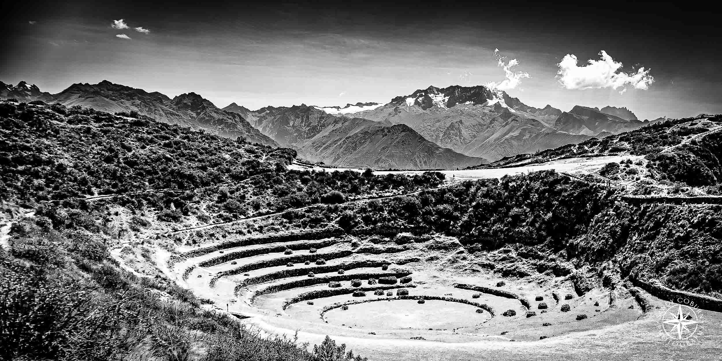 The terraces dip like a crater beneath a jagged road, while an off-center peak holds the frame in quiet tension. The land see