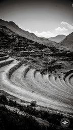 A dramatic black and white photograph of Incan terraces sweeping in a curve across the frame, with shadowed ridges, distant m