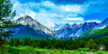An emerald-green meadow in Banff’s Johnston Canyon contrasts with snow-capped mountains under a blue sky with puffy white c