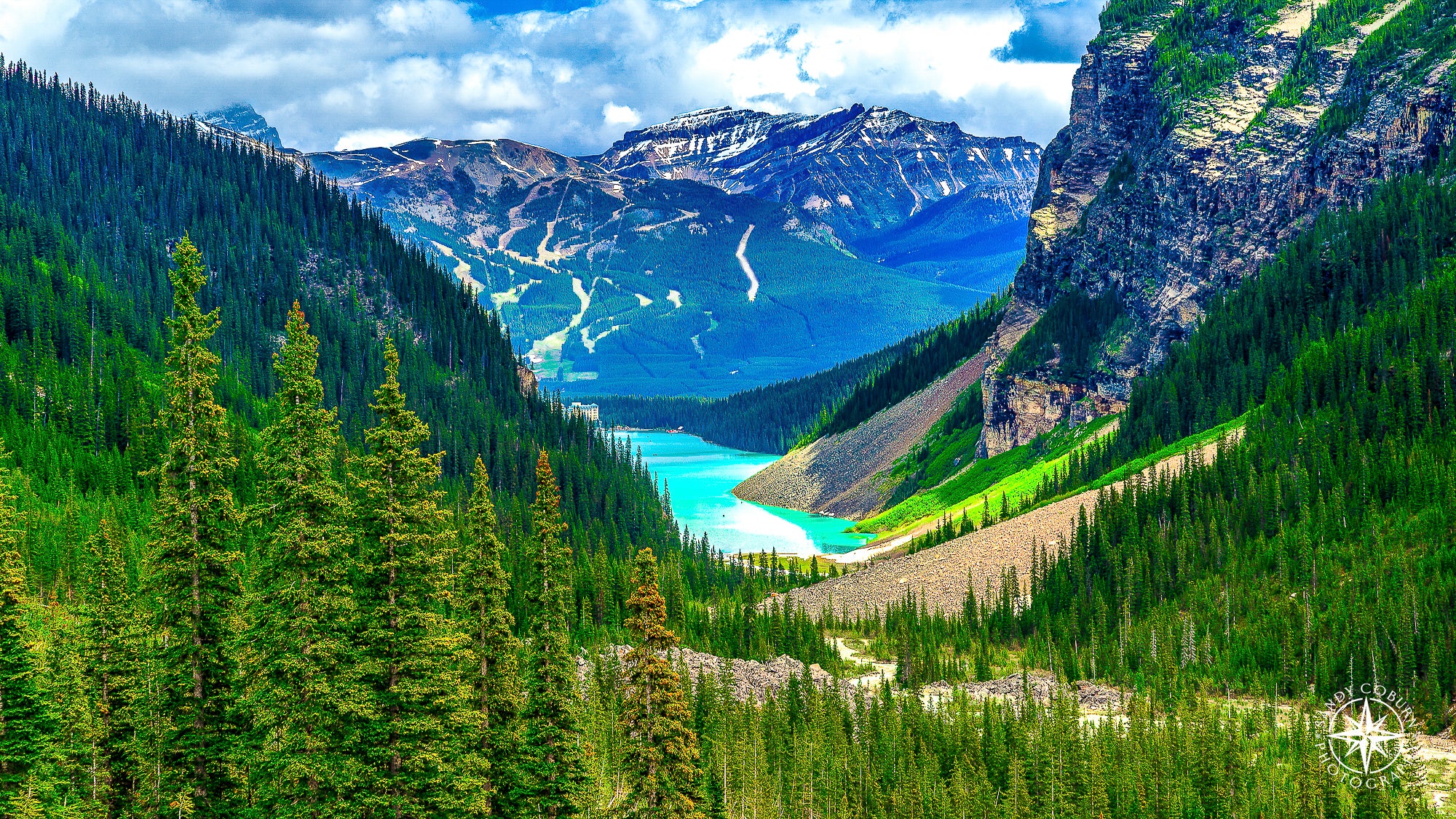 View from a glacier overlooking Lake Louise in Banff National Park, with a snow-capped mountain rising behind and the bright 