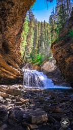 Waterfall framed by curved canyon light in Johnston Canyon, Banff National Park. A distant figure with a camera stands in the