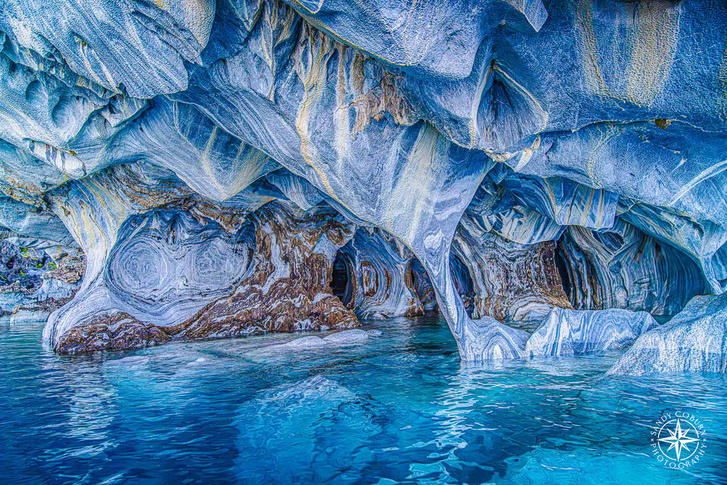 Interior view of a marble cave with blue, white, and ochre patterns reflecting in the water.