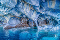 Interior view of a marble cave with blue, white, and ochre patterns reflecting in the water.
