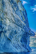 Marble cave wall with a naturally formed rock formation resembling a sculpted human face, overlooking a glacial lake.
