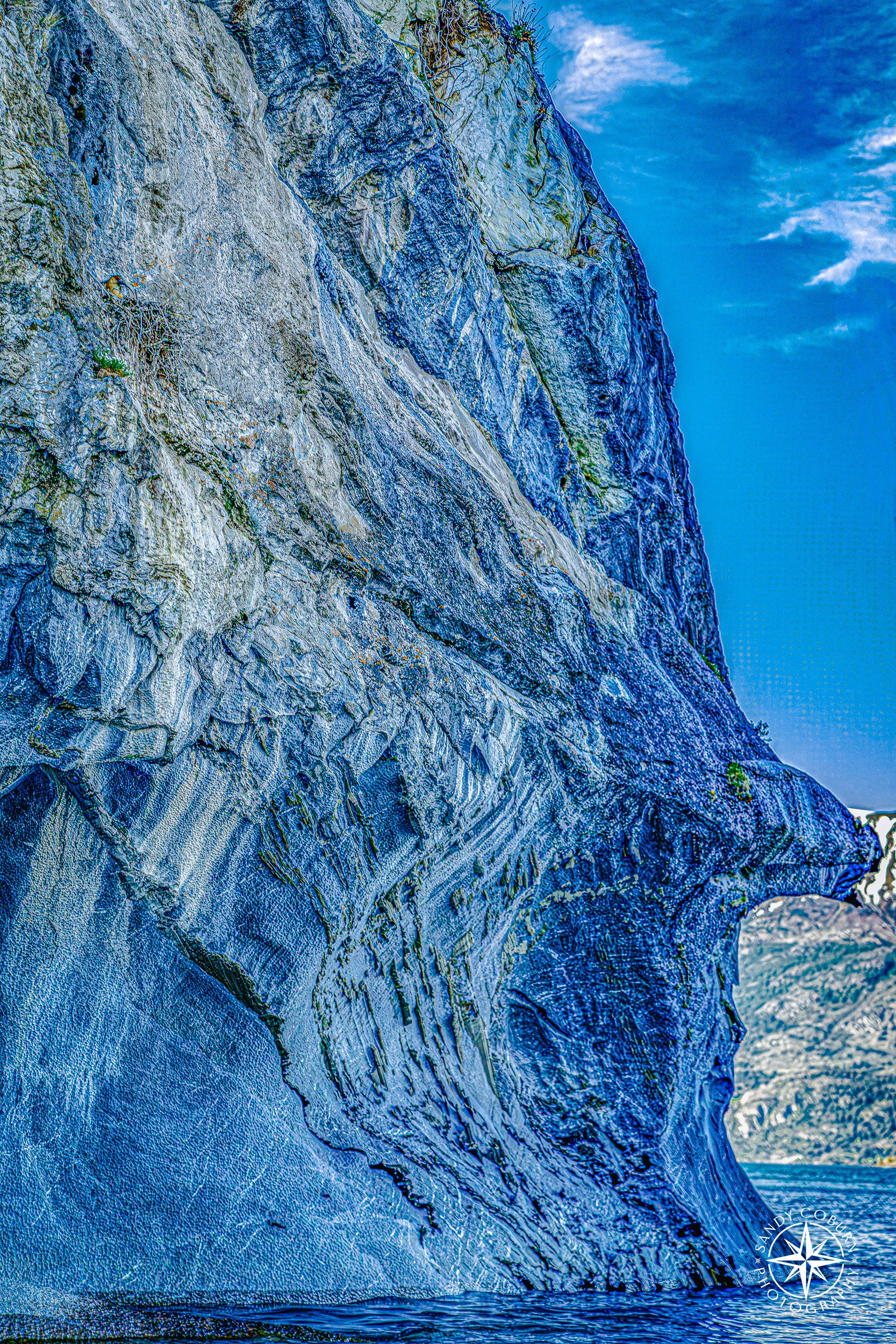 Marble cave wall with a naturally formed rock formation resembling a sculpted human face, overlooking a glacial lake.