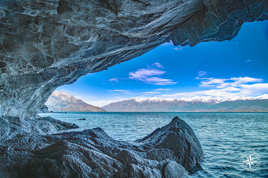 Marble cave opening with tooth-like arches and mountain peaks framed in the distance.