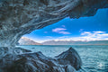 Marble cave opening with tooth-like arches and mountain peaks framed in the distance.