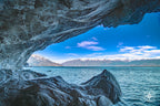 Marble cave opening with tooth-like arches and mountain peaks framed in the distance.