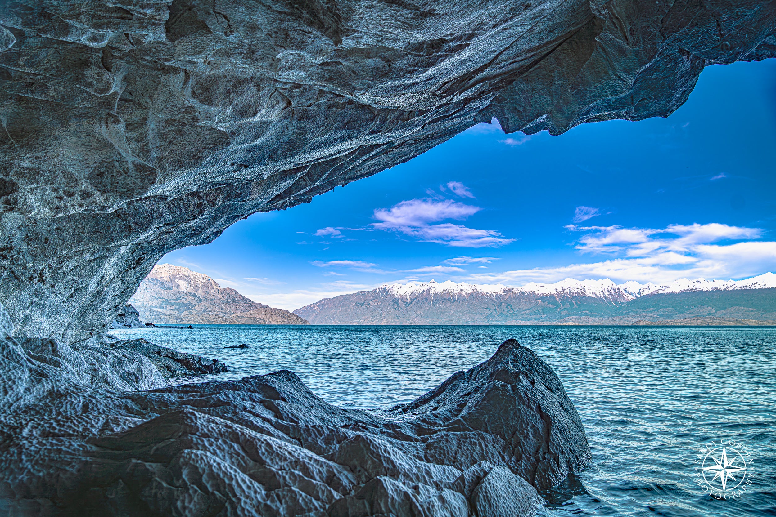 Marble cave opening with tooth-like arches and mountain peaks framed in the distance.