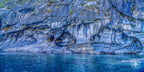 Marble cave with a teardrop-shaped opening and ice-blue mineral veins, overlooking a glacial lake.