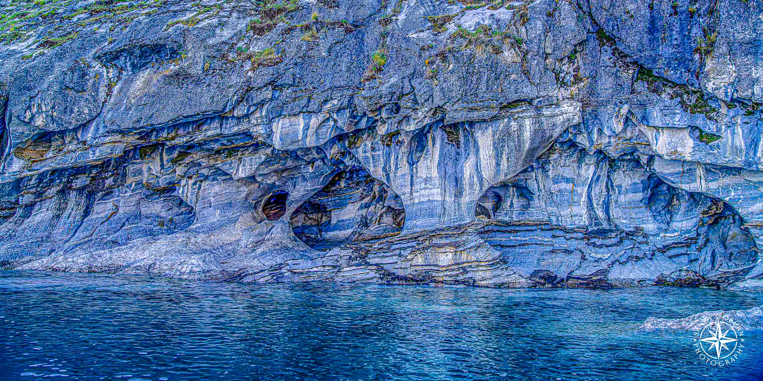 Marble cave with a teardrop-shaped opening and ice-blue mineral veins, overlooking a glacial lake.