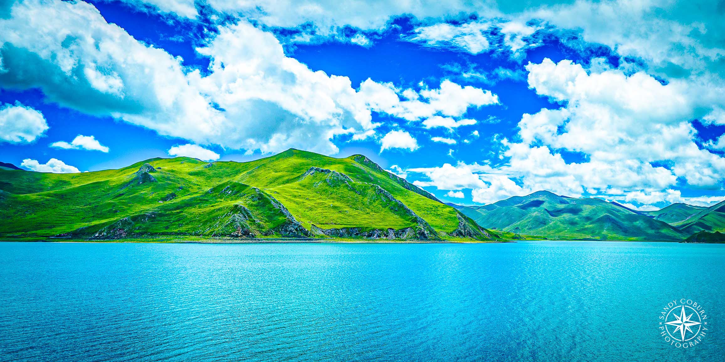 Glacial lake with turquoise water surrounded by green mountains under a partly cloudy sky.