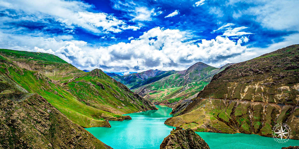 Glacial river winding through steep green Himalayan mountains beneath a vibrant blue sky.