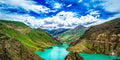 Glacial river winding through steep green Himalayan mountains beneath a vibrant blue sky.