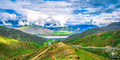 Expansive view of green valleys and rolling hills under long, fast-moving clouds in the Tibetan Plateau.