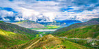 Expansive view of green valleys and rolling hills under long, fast-moving clouds in the Tibetan Plateau.
