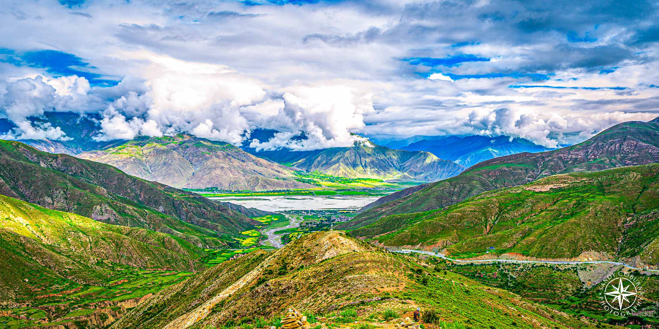 Expansive view of green valleys and rolling hills under long, fast-moving clouds in the Tibetan Plateau.